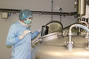 Lady in cleanroom clothing weighs a liquidation approach in a large metal mixing container.