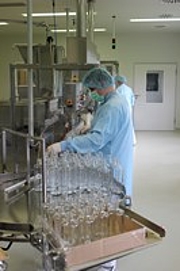 Man in cleanroom garments preparing bottles before bottling to a filling line.
